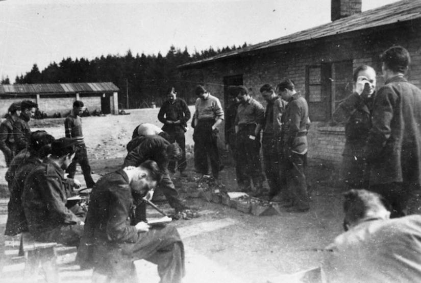 Stalag Fallingbostel, Germany 1944, "This ceremony is the dividing up of swede peelings - mostly rotten, from the German mess. Each man represents a barrack of 80 prisoners fo war and stands in front of the cardboard box into which their share is put.",