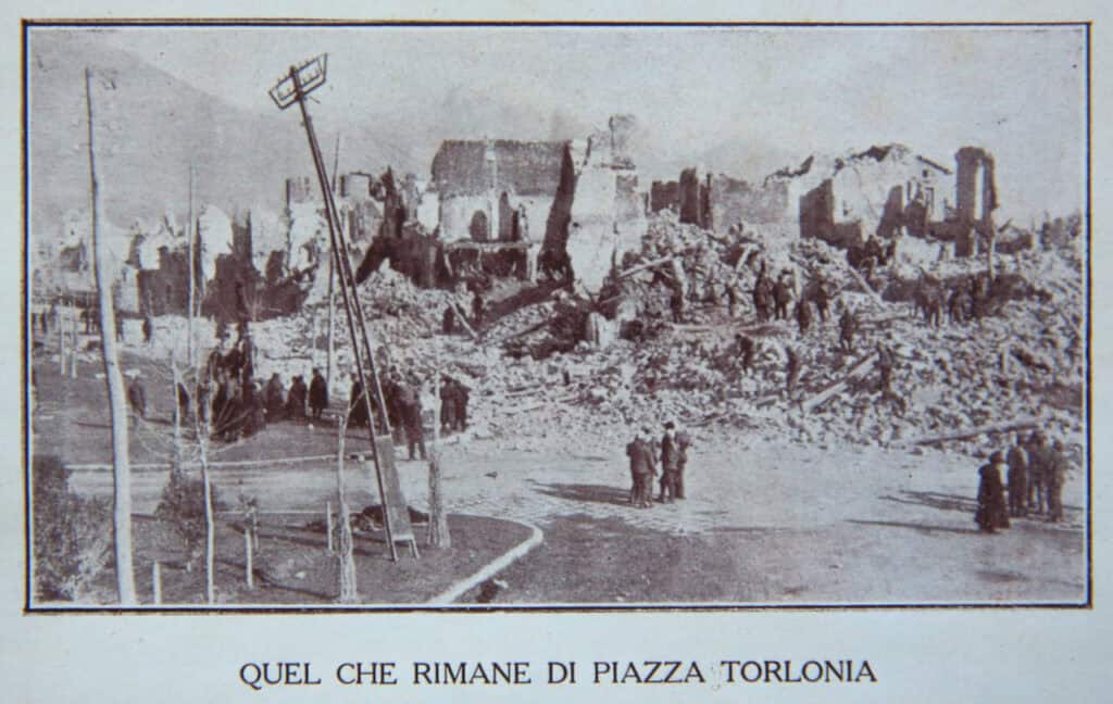 Sepia-toned photo of Piazza Torlonia ruins with damaged buildings and debris.