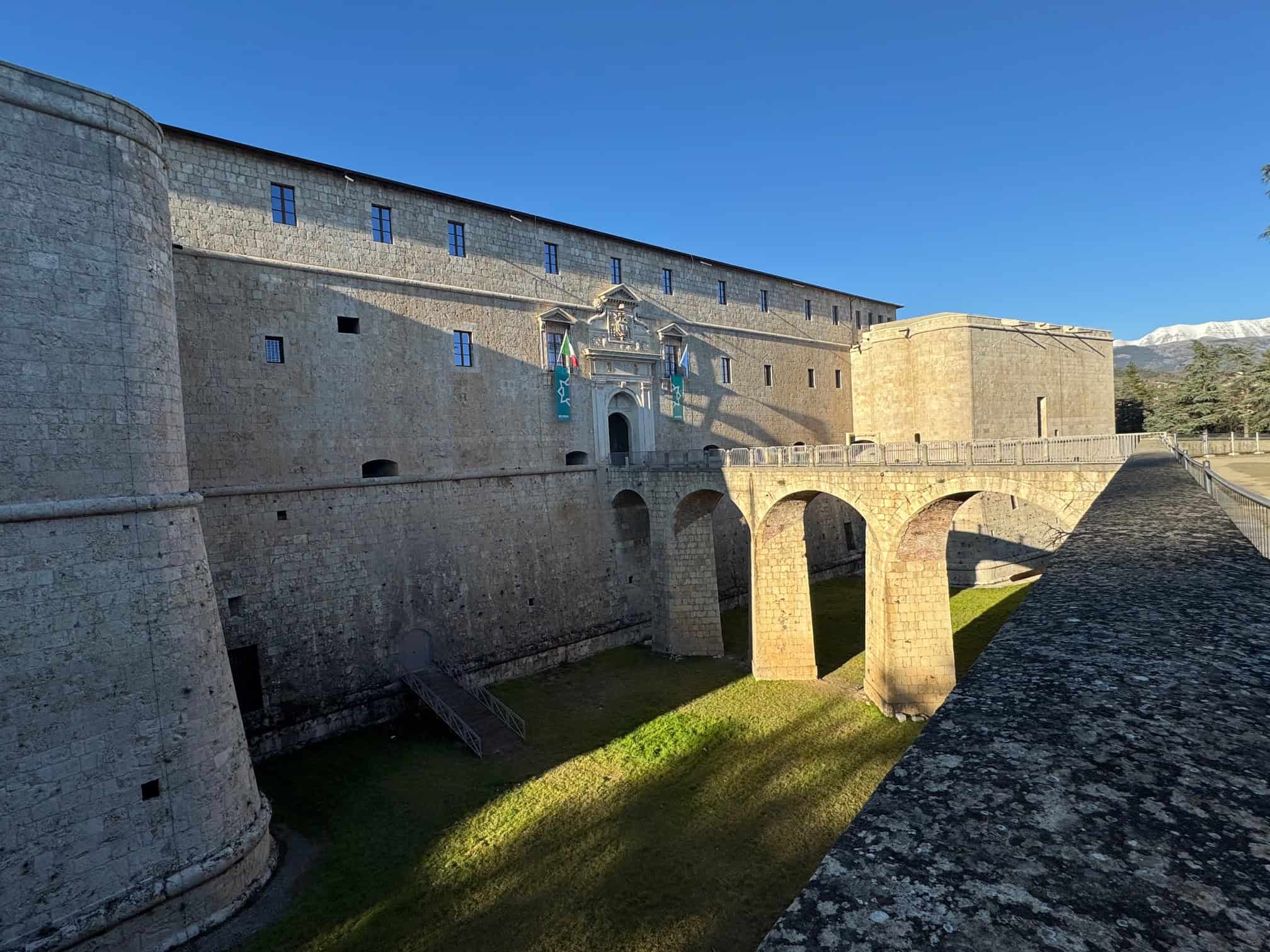 Ancient Abruzzo castle featuring stone architecture and scenic mountain backdrop under clear blue sky.