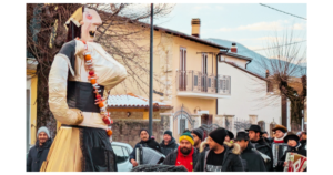 Colorful Abruzzo festival scene featuring a giant puppet and local musicians in a village setting.
